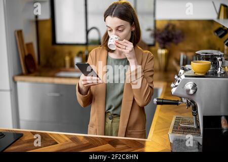 Junge Frau in Eile, um am Morgen zu arbeiten, trägt Jacke, trinkt Kaffee und plaudert unterwegs am Telefon. Tägliche Routine der Geschäftsfrau. Stockfoto