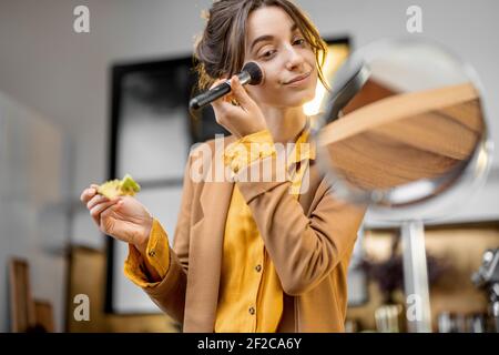 Pingelige junge Geschäftsfrau in Eile, um am Morgen zu arbeiten, Frühstück zu essen und sich unterwegs schminken Stockfoto