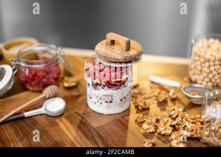 Gesundes Frühstück mit Müsli aus Glas mit Himbeere und Bio-Joghurt auf Holzplatte in der Küche mit Nüssen auf dem Hintergrund. Stockfoto