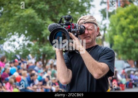 8-31-2019 Tahlequah USA Ältere professionelle Fotografin mit Kappe nach hinten gedreht Und stubbly Schnurrhaare schielt in den Sucher einer großen Videokamera Zoll Stockfoto