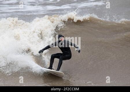 Ein Surfer am Coney Beach, Porthcawl bei Flut und starken Winden von 67mph trifft die South Wales Coast am 11th. März 2021. Kredit: Lewis Mitc Stockfoto