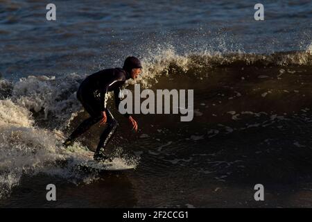 Ein Surfer am Coney Beach, Porthcawl bei Flut und starken Winden von 67mph trifft die South Wales Coast am 11th. März 2021. Kredit: Lewis Mitc Stockfoto