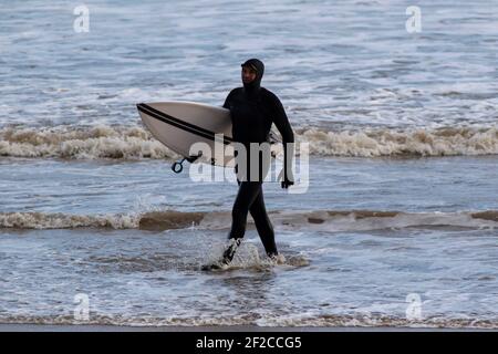 Ein Surfer am Coney Beach, Porthcawl bei Flut und starken Winden von 67mph trifft die South Wales Coast am 11th. März 2021. Kredit: Lewis Mitc Stockfoto