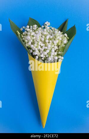 Lilien des Tales in einem gelben Kegel auf dem blauen Hintergrund.Draufsicht.Copy space.Frühling Blumen Konzept. Stockfoto