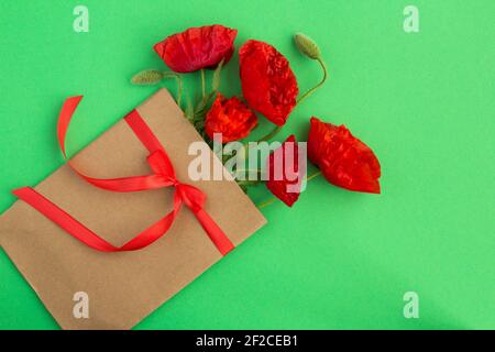 Rote Mohnblumen in einem Umschlag mit einem roten Band auf dem grünen Hintergrund gebunden.Draufsicht.Copy Raum.Frühling oder Sommer Blumen Konzept. Stockfoto