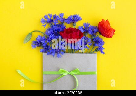 Bouquet von roten Mohnblumen und blauen Kornblumen in einem Umschlag Gebunden mit einem grünen Band auf dem gelben Hintergrund.Draufsicht.Kopieren Raum.Frühling oder Sommer flowe Stockfoto