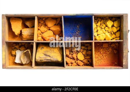 Alte Holzschublade mit Fächern mit blauen, gelben und orangen Pigmenten und getrockneten Farbstoffen, die für einen Maler mit Öl gemischt werden sollen, auf Weiß Stockfoto