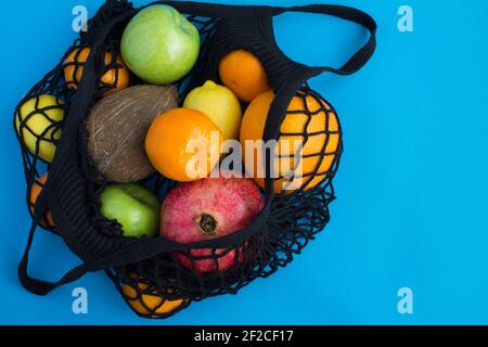 Kein Plastikbeutel-Konzept. Mesh Shopping schwarze Tasche mit verschiedenen Früchten auf dem blauen Hintergrund. Draufsicht. Speicherplatz kopieren. Stockfoto