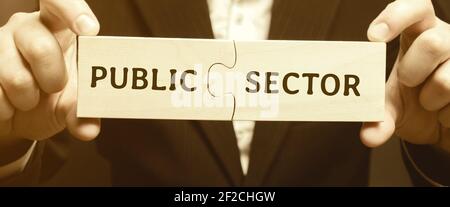 Geschäftsmann stellt zusammen Holzpuzzles mit den Worten Public Sector. Unternehmen, Organisationen und Institutionen, die sich im Besitz staatlicher Stellen befinden und von staatlichen Stellen betrieben werden. Stockfoto