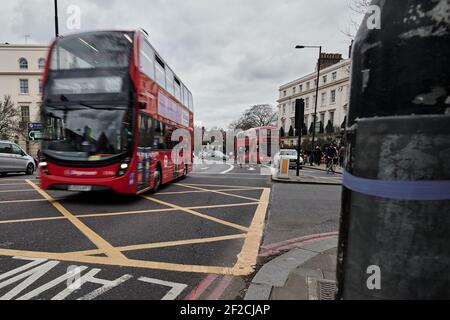 LondonUK - 6 Mär 2021: Bewegungsunschärfe des modernen roten londoner Doppeldeckerbusses, der durch eine geschäftige Kreuzung über eine gelbe gehashte Box fährt Stockfoto