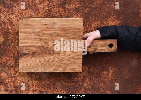 Rustikales Holz Schneidebrett in der Hand auf korrodiertem Metall gehalten Texturierter Hintergrund-Copyspace Stockfoto