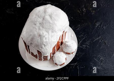Hausgemachte handgemachte Osterkuchen, bedeckt mit weißer Glasur, auf einem Teller auf dunklem Hintergrund. Stockfoto