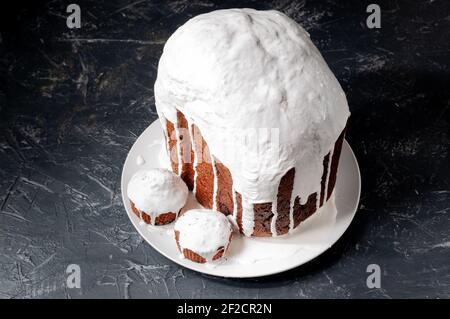Hausgemachte handgemachte Osterkuchen, bedeckt mit weißer Glasur, auf einem Teller auf dunklem Hintergrund. Stockfoto