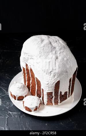 Hausgemachte handgemachte Osterkuchen, bedeckt mit weißer Glasur, auf einem Teller auf dunklem Hintergrund. Stockfoto