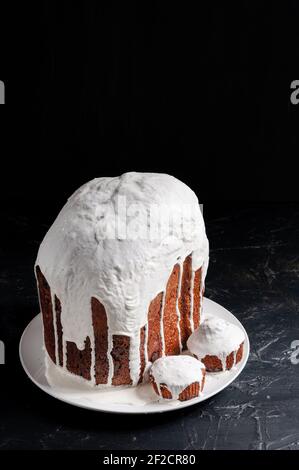 Hausgemachte handgemachte Osterkuchen, bedeckt mit weißer Glasur, auf einem Teller auf dunklem Hintergrund. Stockfoto