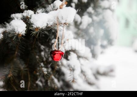 Eine selektive Fokusaufnahme einer roten Glocke, die hängt Auf einer Fichte, die im Winter mit Schnee bedeckt ist Stockfoto