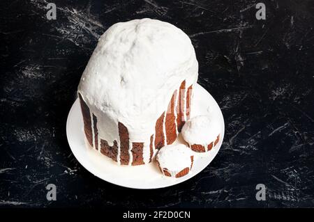 Hausgemachte handgemachte Osterkuchen, bedeckt mit weißer Glasur, auf einem Teller auf dunklem Hintergrund. Stockfoto