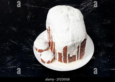 Hausgemachte handgemachte Osterkuchen, bedeckt mit weißer Glasur, auf einem Teller auf dunklem Hintergrund. Stockfoto