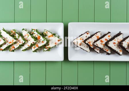 Schöne Snacks von weichem Frischkäse auf einem weißen Teller auf grünem Hintergrund. Hüttenkäse-Snacks mit Lachs und Kräutern. Stockfoto