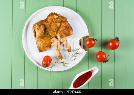 Hühnertabak mit Tomatensauce, Rosmarin und Tomaten auf einem schönen weißen Teller auf grünem Hintergrund. Gegrilltes Hähnchen. Stockfoto