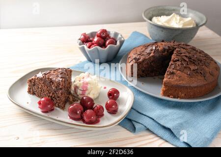 Hausgemachte Schokoladenkuchen mit Morello Kirschen und Schlagsahne auf einer blauen Serviette und einem hellen Holztisch, Kopierraum, ausgewählter Fokus, enge Tiefe o Stockfoto