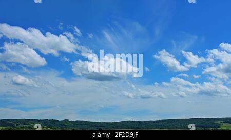 Wunderschöne Wolkenlandschaft über einer bewaldeten hügeligen Landschaft in schönen Sommertag, Cumulus und Cirrus weißen Wolken, lebendigen blauen Himmel Stockfoto