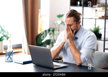 Kaukasischen ungesunden Mann Gefühl schlecht, krank mit laufender Nase, brauchen einen Rest.Male Manager oder Freiberufler sitzen am Schreibtisch im Home Office, arbeiten entfernt, mit Papiertaschentuch, Niesen Stockfoto