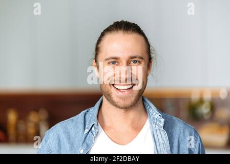 Porträt eines schönen attraktiven kaukasischen Kerl, Student oder Freiberufler. Stilvoller junger Mann im Jeanshemd, der freundlich in der Kamera aussieht und lächelt und drinnen steht Stockfoto