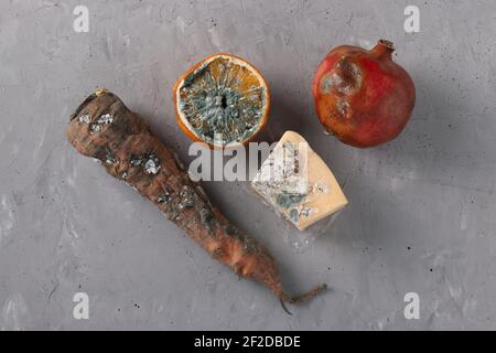 Verdorbene verfaulte Lebensmittel mit Schimmel: Halbe Orange, Granatapfel, Karotten und Hartkäse auf grauem Hintergrund, Draufsicht Stockfoto