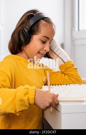 Kleine kaukasische Mädchen, mit einem Guss in einer Hand, trägt ein gelbes Sweatshirt, Skizzen an ihrem Schreibtisch sehr glücklich und lächelnd, mit Zeichenmaterial Stockfoto