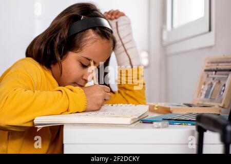 Kleine kaukasische Mädchen, mit einem Guss in einer Hand, trägt ein gelbes Sweatshirt, Skizzen an ihrem Schreibtisch sehr glücklich und lächelnd, mit Zeichenmaterial Stockfoto