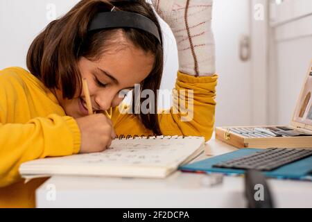 Kleine kaukasische Mädchen, mit einem Guss in einer Hand, trägt ein gelbes Sweatshirt, Skizzen an ihrem Schreibtisch sehr glücklich und lächelnd, mit Zeichenmaterial Stockfoto