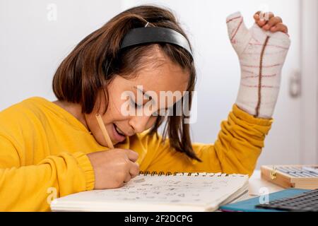 Kleine kaukasische Mädchen, mit einem Guss in einer Hand, trägt ein gelbes Sweatshirt, Skizzen an ihrem Schreibtisch sehr glücklich und lächelnd, mit Zeichenmaterial Stockfoto