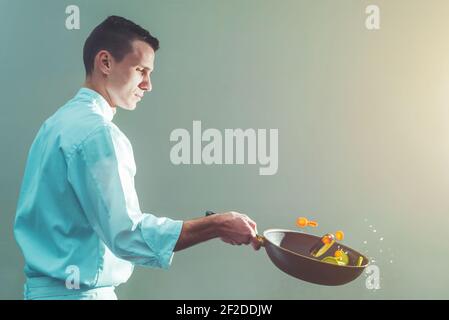 Professioneller junger Koch, der Gemüse in einer Bratpfanne zubereitet und dreht, professionelles Kochkonzept mit Kopierfläche Stockfoto