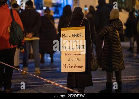 Frau tragt Schild: ' Meine Enkel und meine 99-jährige Tante leiden massiv an den Maßnahmen '. Am 11. März 2021, ein Jahr nach der Ausrufung der Covid-19 Pandemie durch die WHO, sammeln sich knapp 100 Menschen in München, um gegen sätliche Corona Maßnahmen zu demontieren. - am 11 2021. März, ein Jahr nachdem die WHO von einer Pandemie gesprochen hatte, nahmen etwa 100 Menschen an einer Demonstration gegen alle Covid-Maßnahmen Teil. (Foto: Alexander Pohl/Sipa USA) Quelle: SIPA USA/Alamy Live News Stockfoto