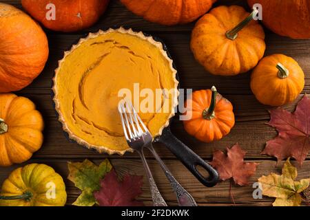 Traditionelle Kürbis Pie flach legen. Offene hausgemachte Kuchen in Gusseisen Pfanne gebacken, umgeben von hellen Kürbissen und marple Blätter auf rustikalem Hintergrund über Stockfoto