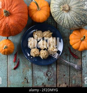 Veganes Gericht. Hausgemachte Manti, traditionelle asiatische gedünstete Knödel in marineblauer Platte mit rohen Kürbissen und Chilischoten auf rustikalem blauem Backgr dekoriert Stockfoto