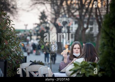 BELGRAD, SERBIEN - 21. FEBRUAR 2021: Junge Leute, zwei junge Mädchen, Freunde, essen in einem Fast-Food-Restaurant mit Gesichtsmaske Schutzausrüstung Stockfoto