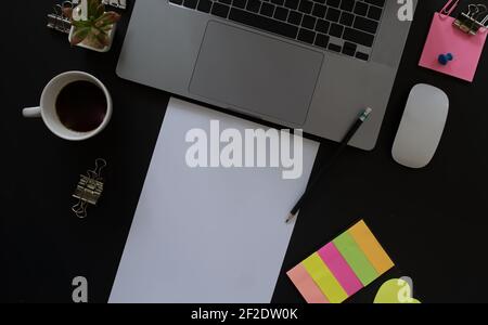 Schreibtisch mit Laptop und Notizpapier auf schwarzem Hintergrund, einschließlich Kopierbereich zum Hinzufügen von Text oder Grafiken. Stockfoto