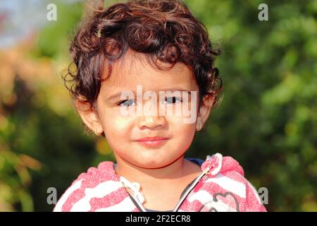 Nahaufnahme Porträt eines kleinen Kindes indischer Herkunft lächelnd im Garten stehend, indien. Konzept für die Kinder von heute morgen die Zukunft, Kindheit mem Stockfoto