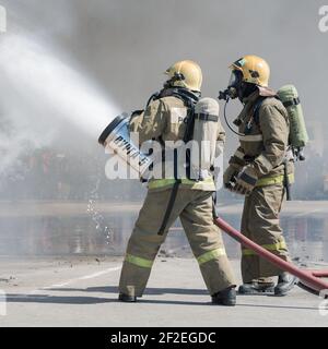 Zwei Feuerwehrleute löschen das Feuer aus dem Löschschlauch mit einem Löschwasserschaumfass mit luftmechanischem Schaum. Professioneller Urlaub Feuerwehrmann Tag Stockfoto