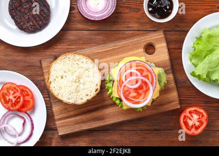 Hausgemachter Hamburger mit Cutlet, Salat, Zwiebel, Tomate und Käse. Cheeseburger, Burger. Schritt für Schritt. Draufsicht. Burger kochen Stockfoto