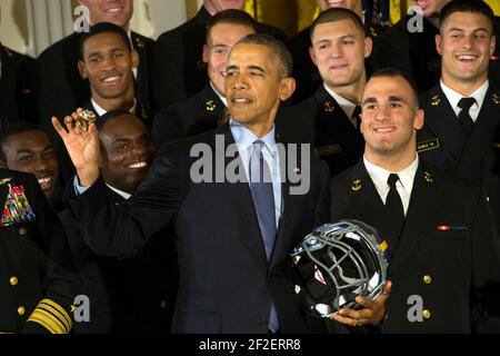 Präsident Barack Obama hält einen Fußballhelm der US Naval Academy, während er einen Mannschaftsring inspiziert. Stockfoto