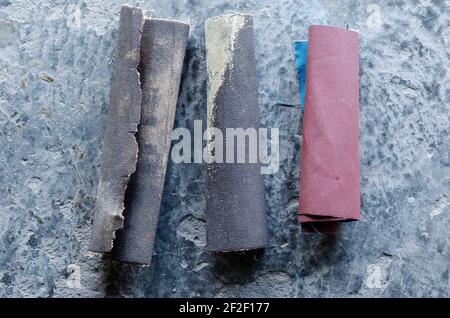 Altes Sandpapier auf einem grauen Betonboden. Drei Rollen Schmirgelpapier auf einer grauen Zementoberfläche. In Innenräumen. Draufsicht. Stockfoto