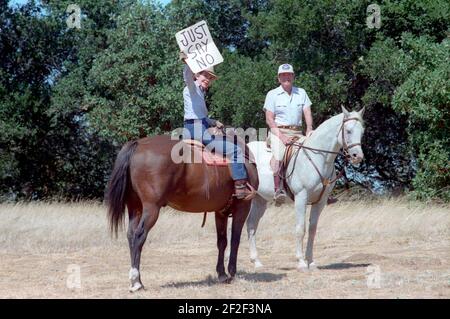 Präsident Ronald Reagan mit Nancy Reagan, die ein Schild "Sag einfach Nein" für Pressefotografen hält, während sie auf Pferden in Rancho Del Cielo reiten. Stockfoto