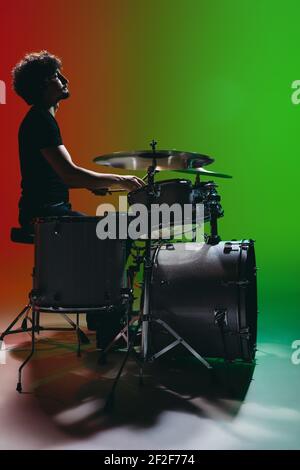Porträt eines jungen Schlagzeugers, der isoliert auf grün-rotem Hintergrund spielt In Neon Stockfoto