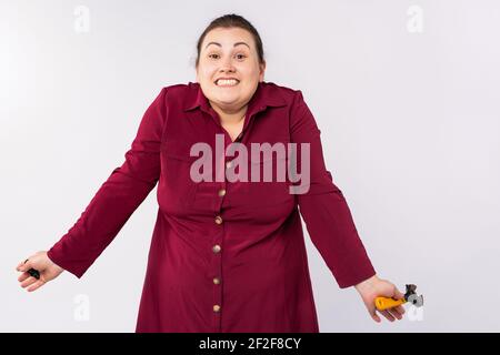 Junge blonde, kaukasische plus size Frau trägt Kleid hält Schlüssel ahnungslos mit verwirrten Ausdruck, Zweifel, Weiblichkeit Konzept. Grauer Hintergrund Stockfoto