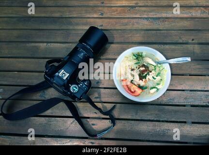 Soto Ayam, traditionelle indonesische Hühnersuppe und eine Kamera auf dem Holztisch Stockfoto