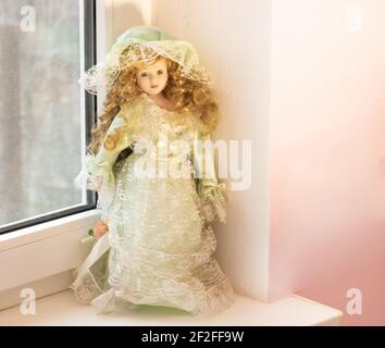 Eine schöne Puppe mit goldenem Haar auf der Fensterbank. Stockfoto