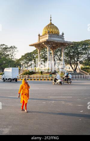 Frau in orange kurta geht an der Kreuzung vor dem Palast in Mysore, Indien Stockfoto